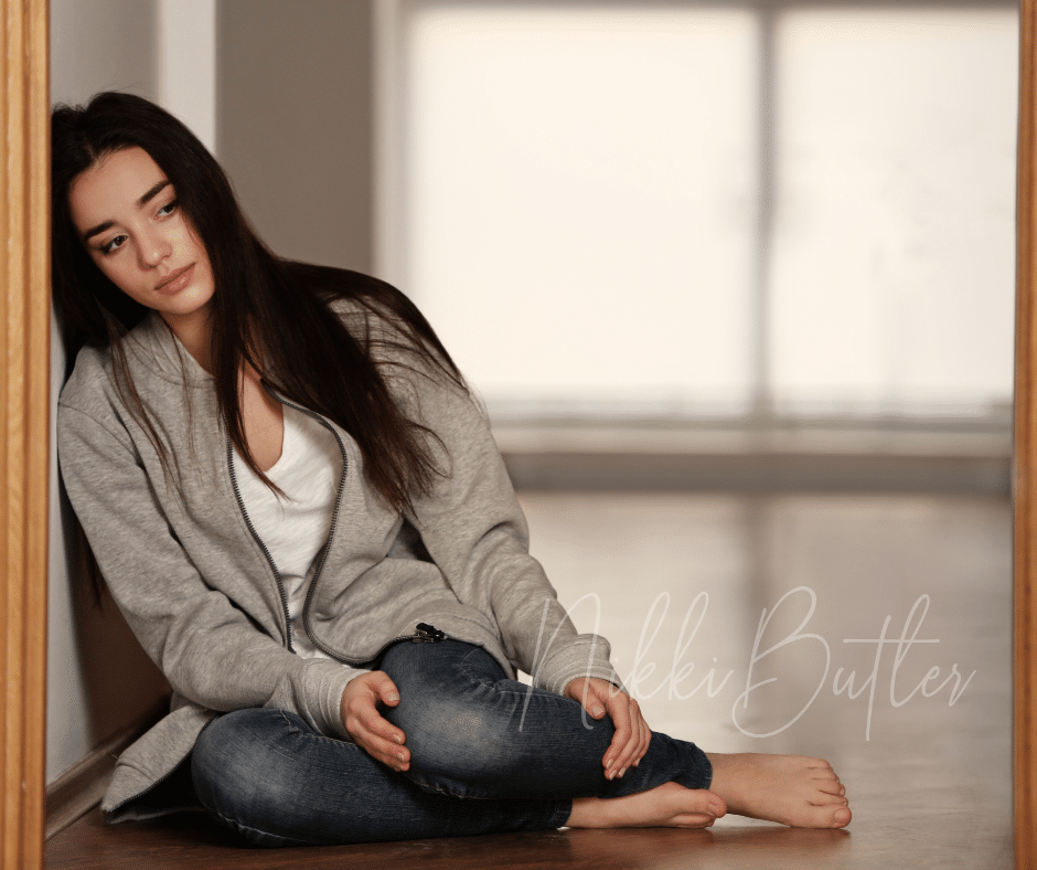 a young woman leaning against a doorframe, sat on the floor, looking sad